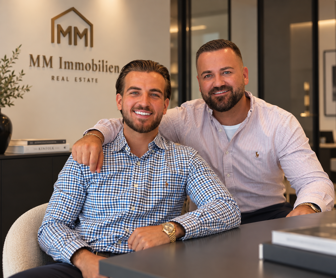 Flori und Mergim von MM Immobilien im Büro vor dem MM Immobilien Logo
